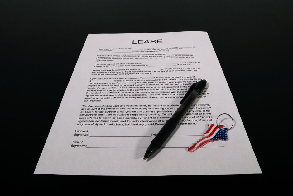 A hand signing a lease agreement document with a pen at a table