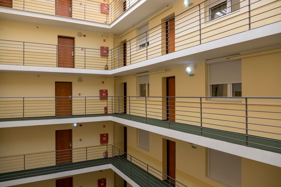 A long carpeted apartment building hallway lined with numbered doors where neighbors pass each other