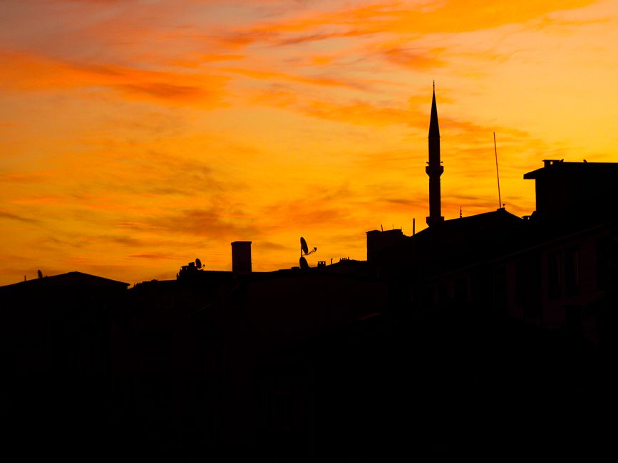 A city skyline at sunset seen from a building rooftop, the kind of view residents gather to watch