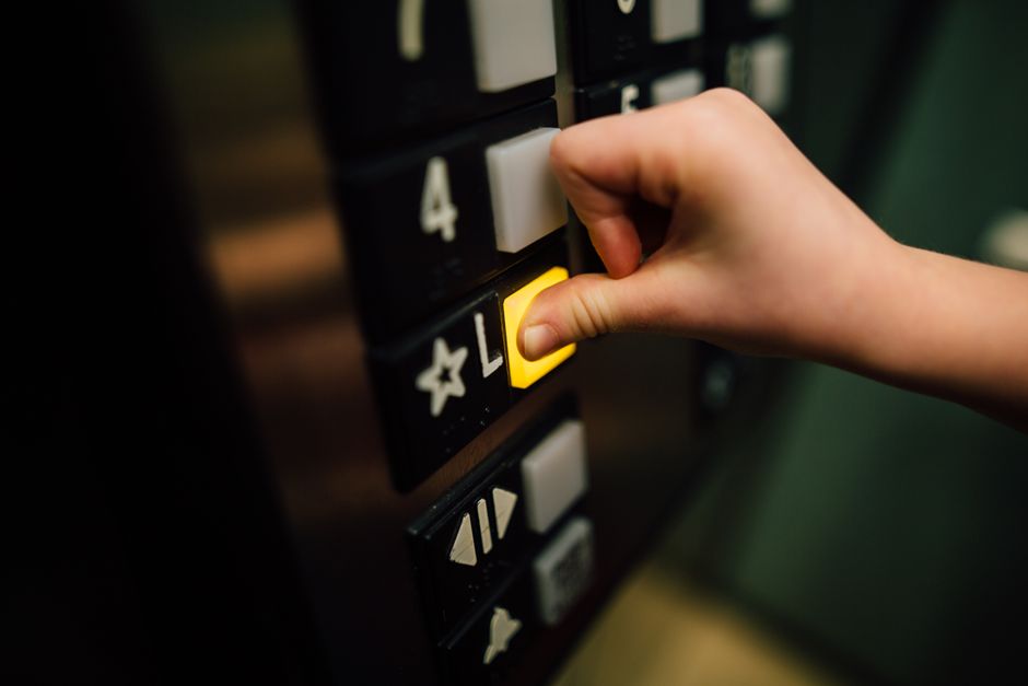 A small child reaching up to press a button inside an apartment building elevator