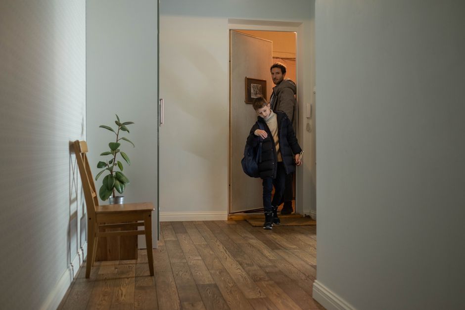 A parent and young child walking together down a carpeted apartment building hallway