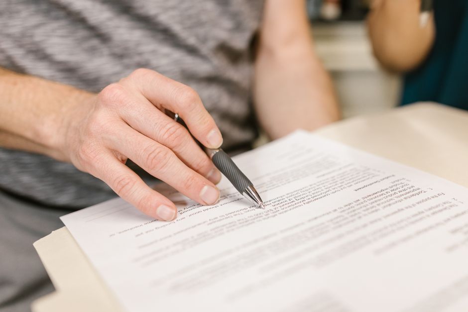 A person reviewing and signing a printed residential lease agreement with a pen at a table