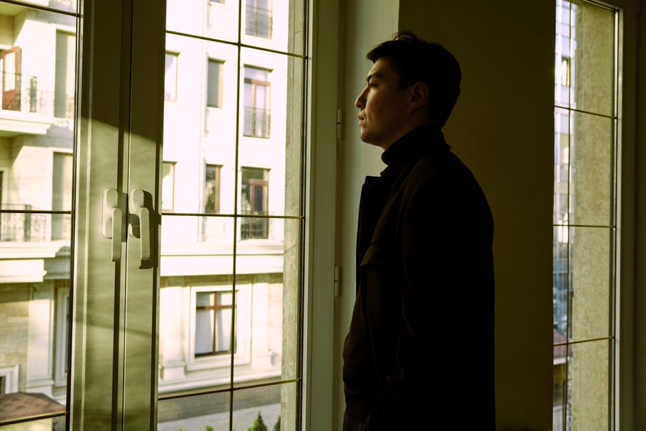 A resident standing at an apartment window at night, quietly observing the street below before deciding whether to act
