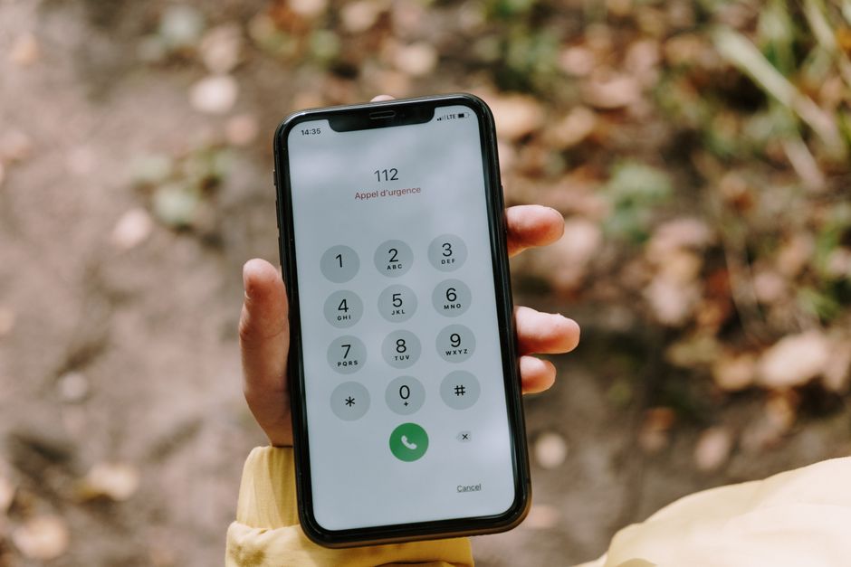 A close-up of a hand holding a smartphone and dialing, choosing the right line to call for the situation