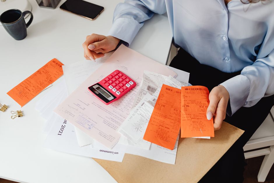 A calculator resting on a stack of bills and paperwork while someone adds up the true monthly cost of renting an apartment