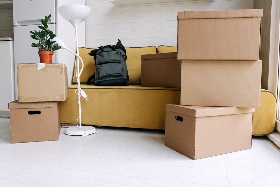 Stacked cardboard moving boxes in an empty apartment ready for a move, illustrating the added cost of relocating