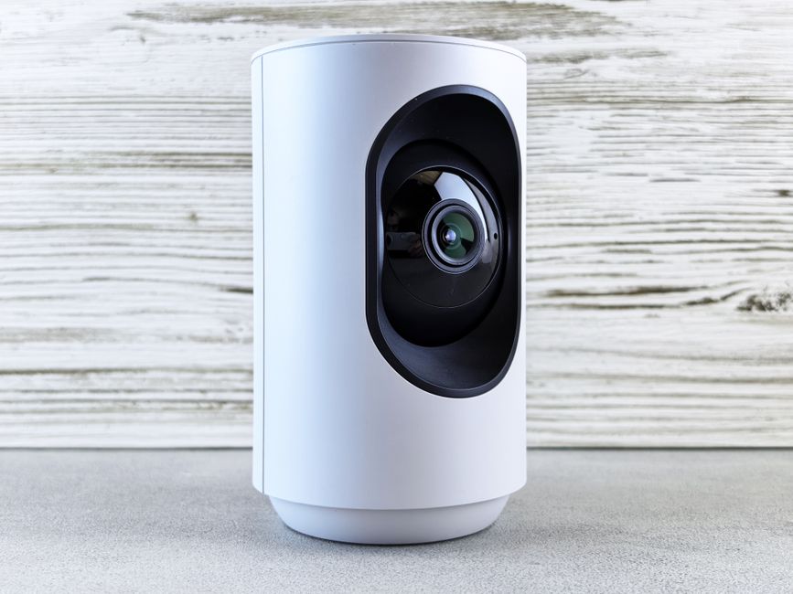 A small indoor home security camera sitting on a shelf facing a living room entry