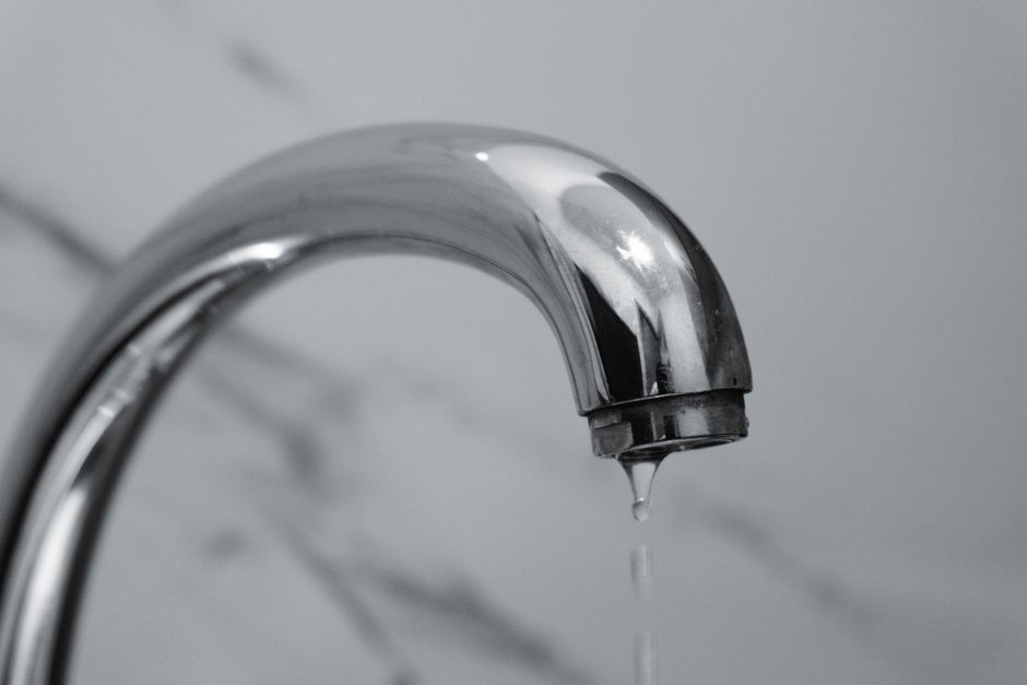 A slow drip from the pipe under a kitchen sink cabinet, the kind of specific problem a well-written repair email describes.