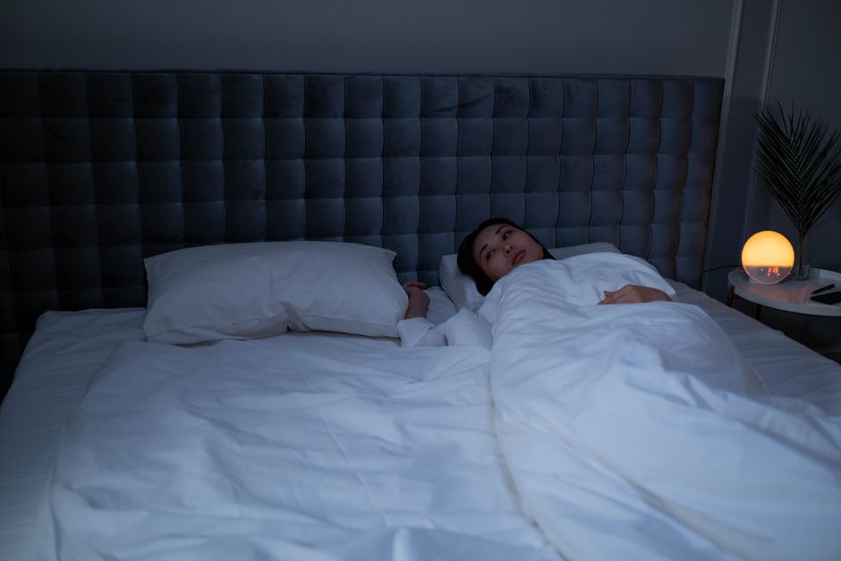 A person lying awake in bed late at night, kept up by noise coming through the apartment wall.