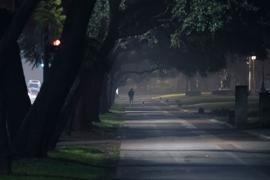 A person walking alone along a well lit city sidewalk at night at a steady, purposeful pace