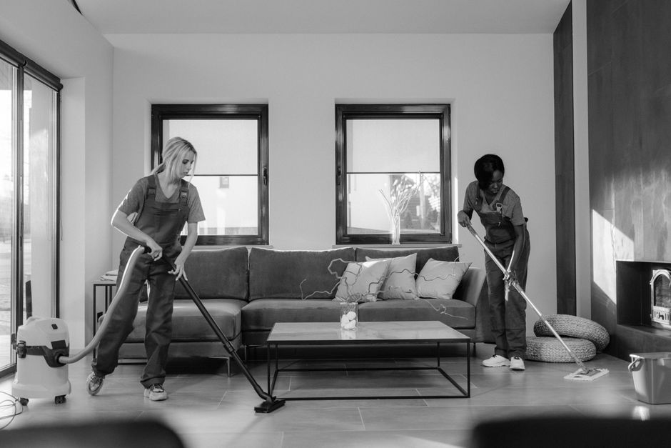 A person running a vacuum cleaner across the floor of an apartment living room during daytime hours.