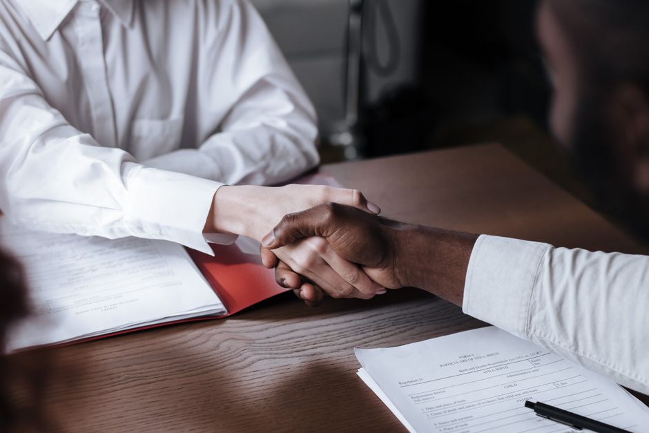 Two people shaking hands across a table after reaching an agreement, representing a resolution worked out through mediation.