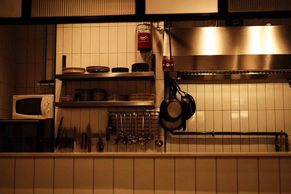 A red fire extinguisher mounted on a wall near an apartment kitchen stove, where most cooking fires start