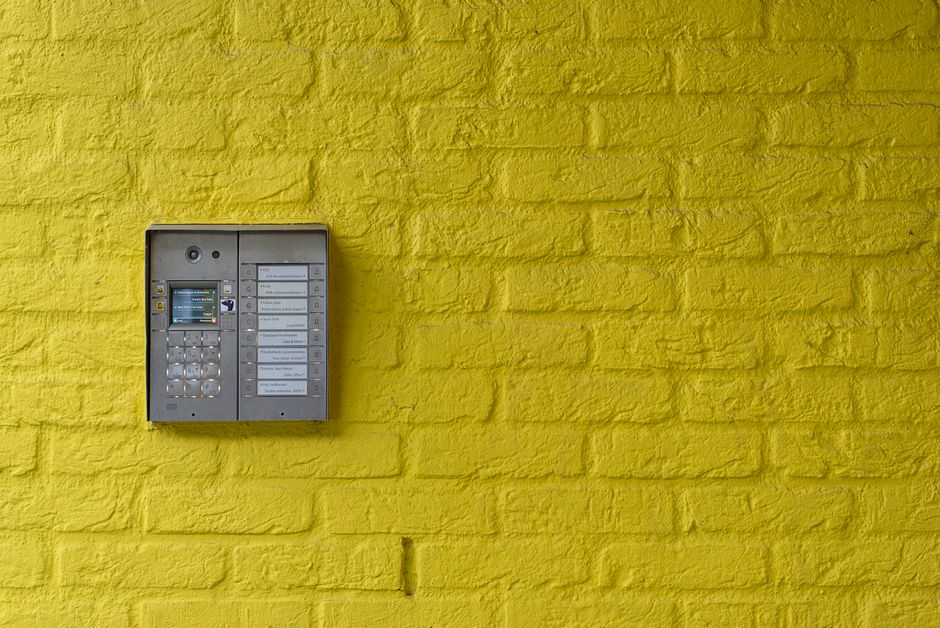 A wall-mounted intercom and buzzer panel at an apartment building entrance where visitors call up to a specific unit.