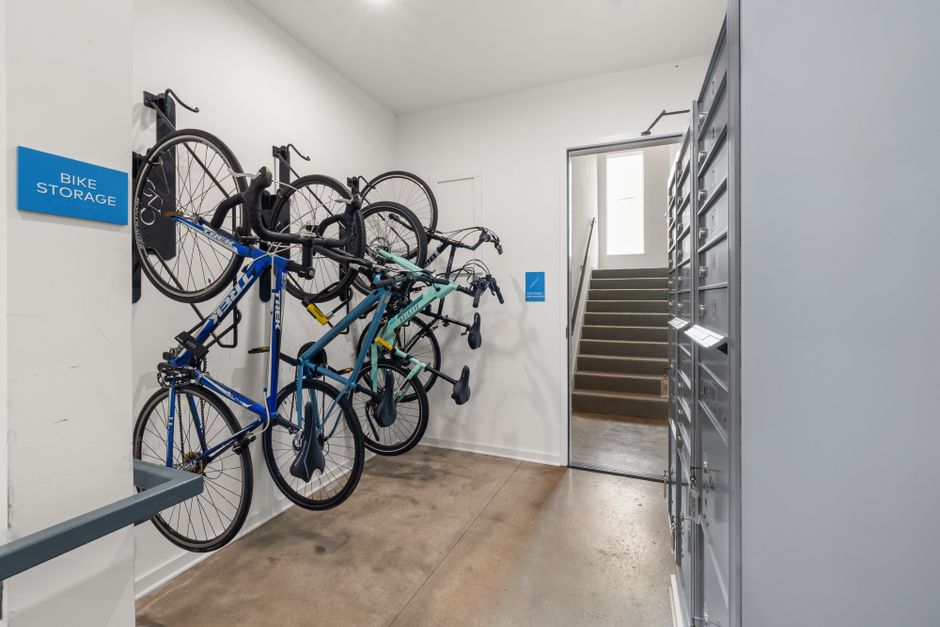 A shared apartment bike room with bicycles parked on floor racks and mounted on wall hooks.