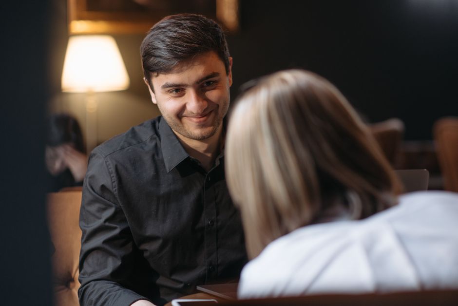 Two people sitting across a small cafe table with coffee cups, having a conversation like a potential roommate screening meet