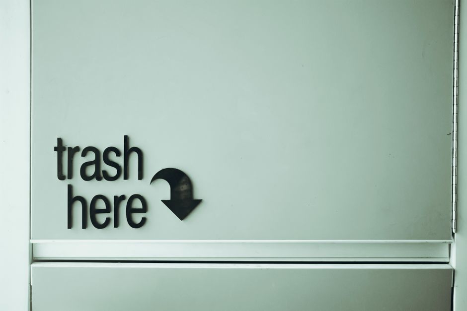 A small metal trash chute hopper door set into an apartment building hallway wall