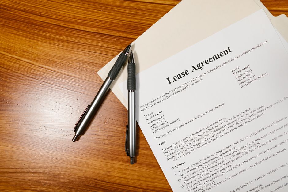 Hands signing a printed housing agreement on a table with a pen, representing a roommate agreement and lease