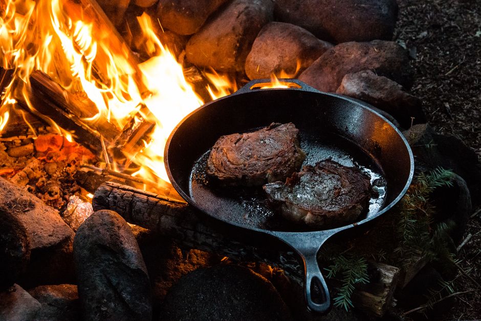 A steak searing in a heavy cast iron pan on a stovetop burner.