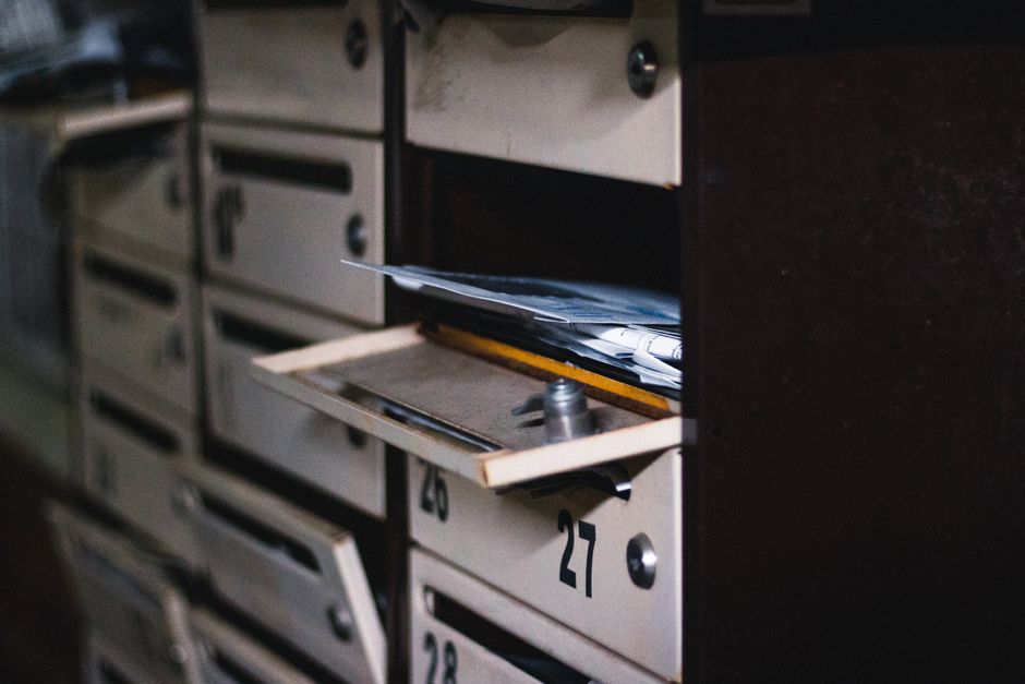 Unopened letters and mail overflowing from an apartment building mailbox, a common sign that a neighbor may not be collecting