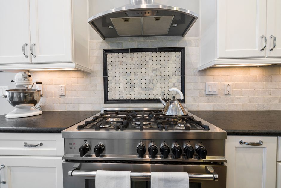 A stainless steel range hood mounted above a stovetop in an apartment kitchen, the kind of exhaust fan that pulls cooking sme