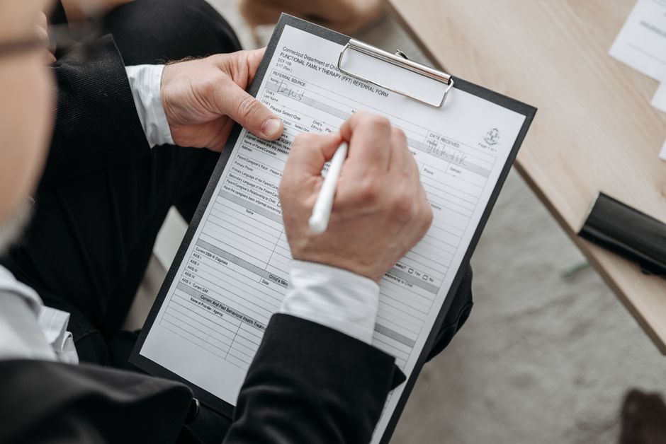 A person signing a printed document on a clipboard with a pen.