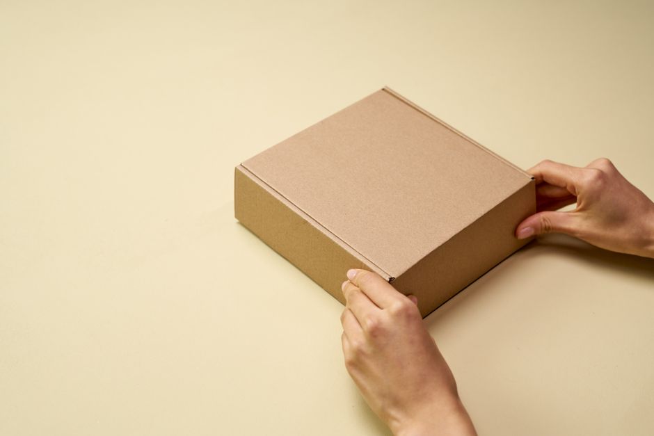 A person carrying a small cardboard box with both hands to return it to a neighbor