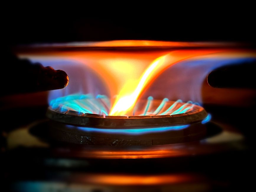 A lit blue flame on a gas stove burner in an apartment kitchen