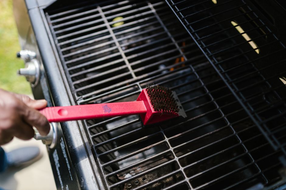 A wire grill brush scrubbing the warm grates of an outdoor gas grill clean