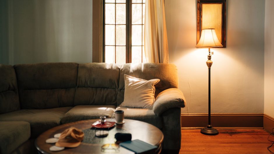 A warm-toned floor lamp glowing beside a couch and rug in a softly lit apartment living room
