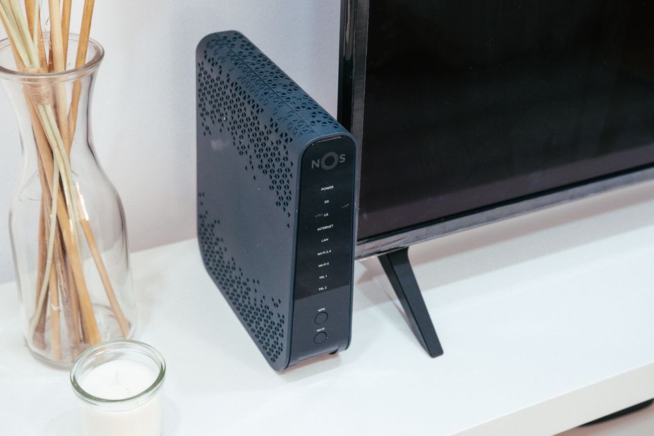 A home wifi router and modem sitting on a wooden desk near a window in an apartment
